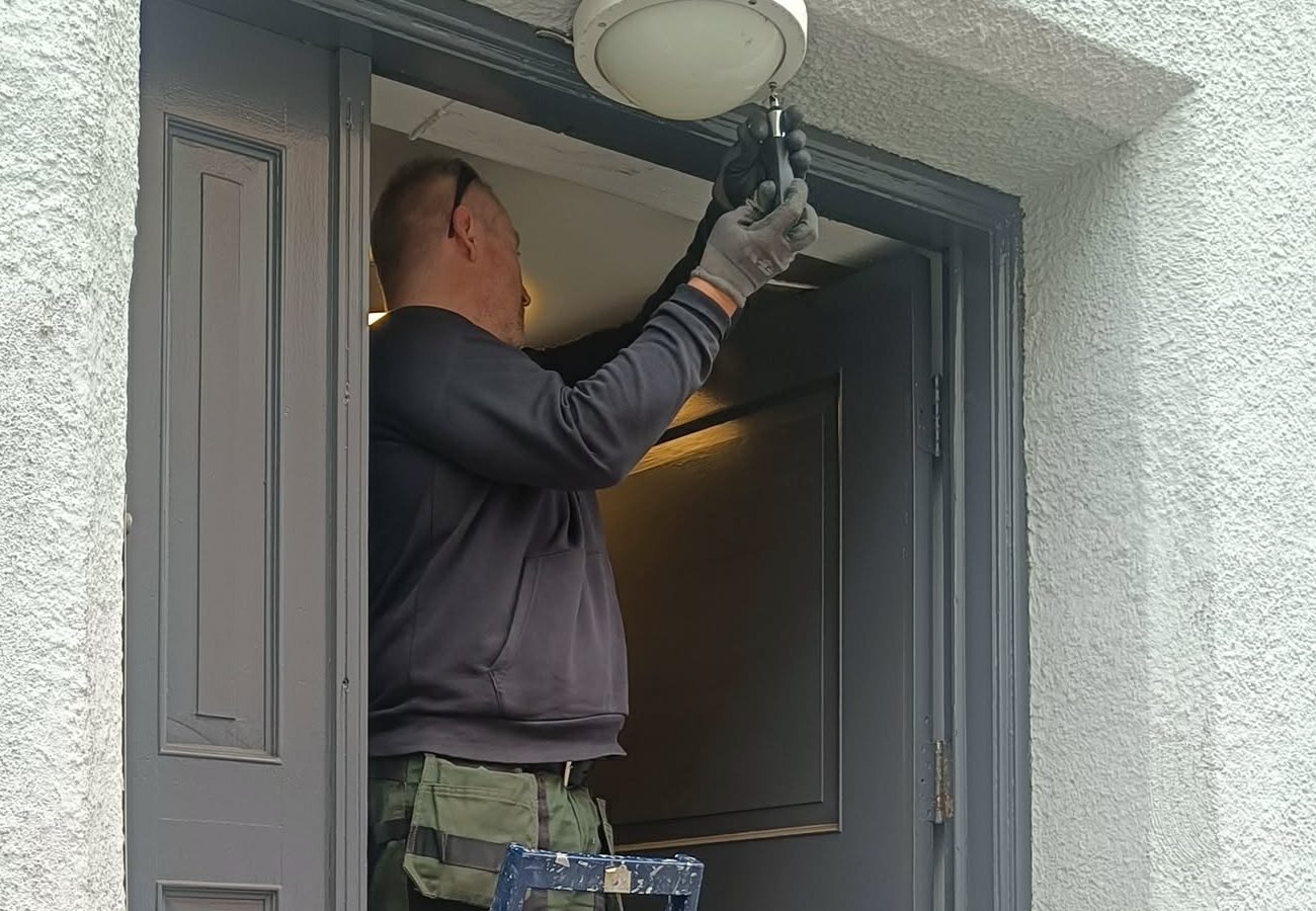 Medarbeider fra Den Hjelpende Hånd bytter lyspære over en inngangsdør