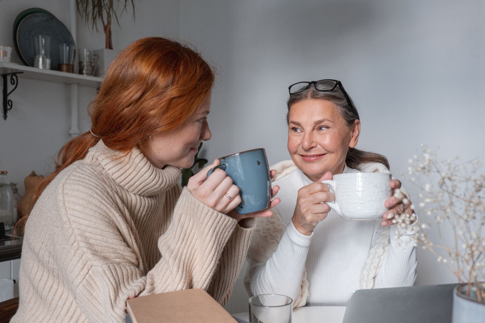 En eldre og en yngre kvinne deler en kaffekopp hjemme ved kjøkkenbordet
